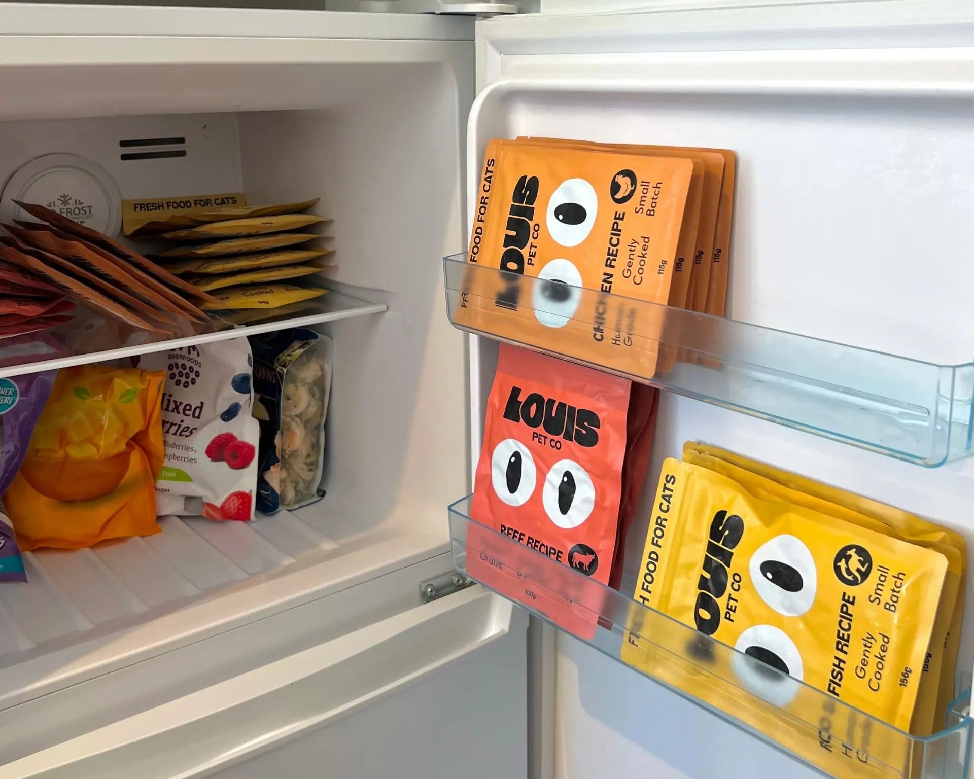 Louis Pet Co fresh cat food pouches neatly stored in a freezer alongside frozen fruit and meals.