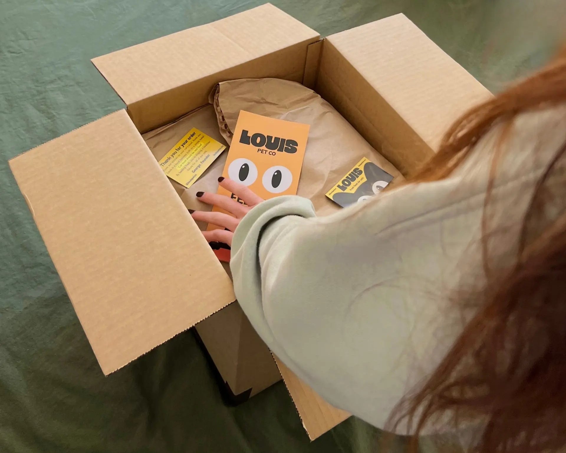 Girl customer unboxing a Louis Pet Co delivery with branded packaging and thank-you cards inside.